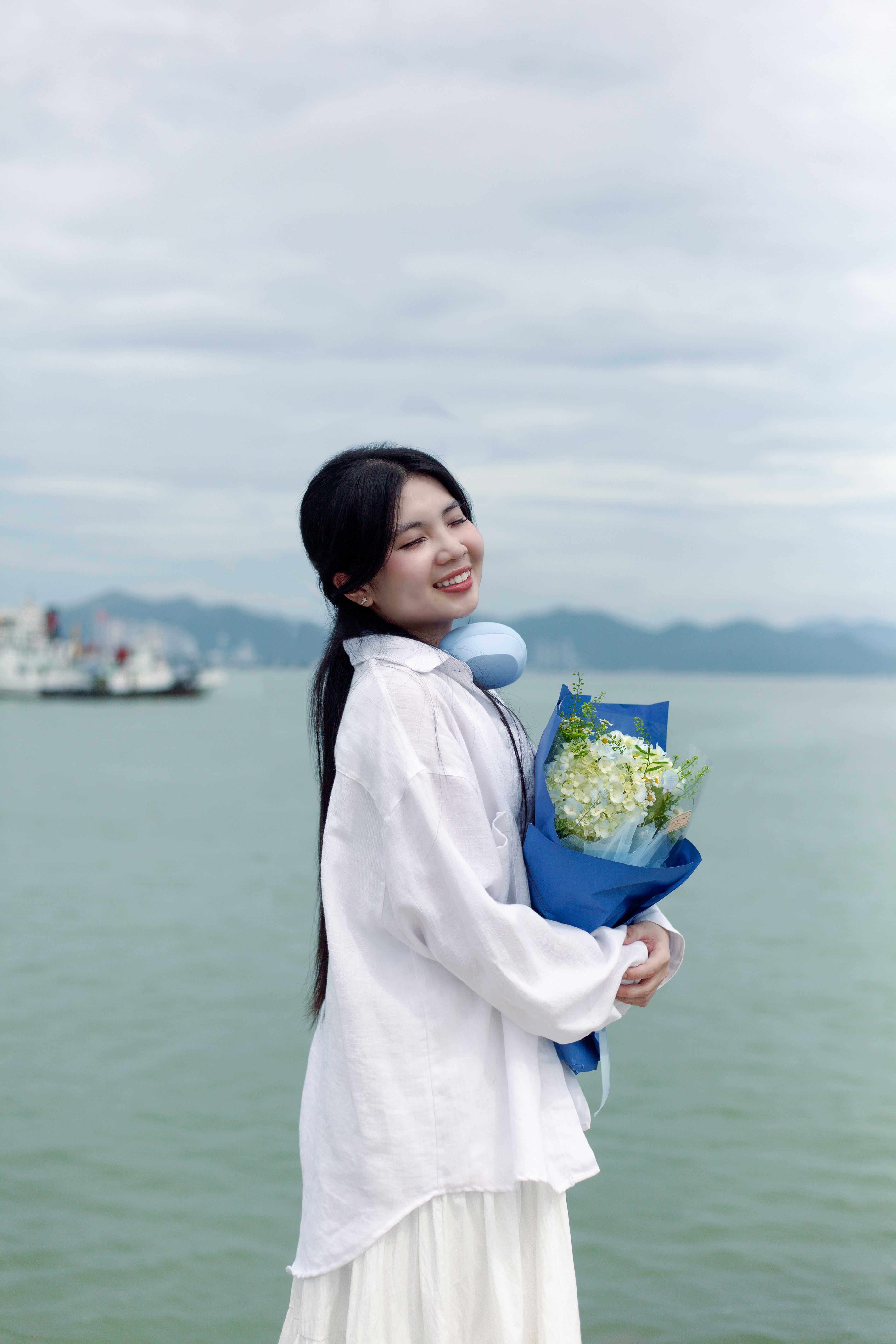 Young Woman Smiling with Flowers by Sea · Free Stock Photo