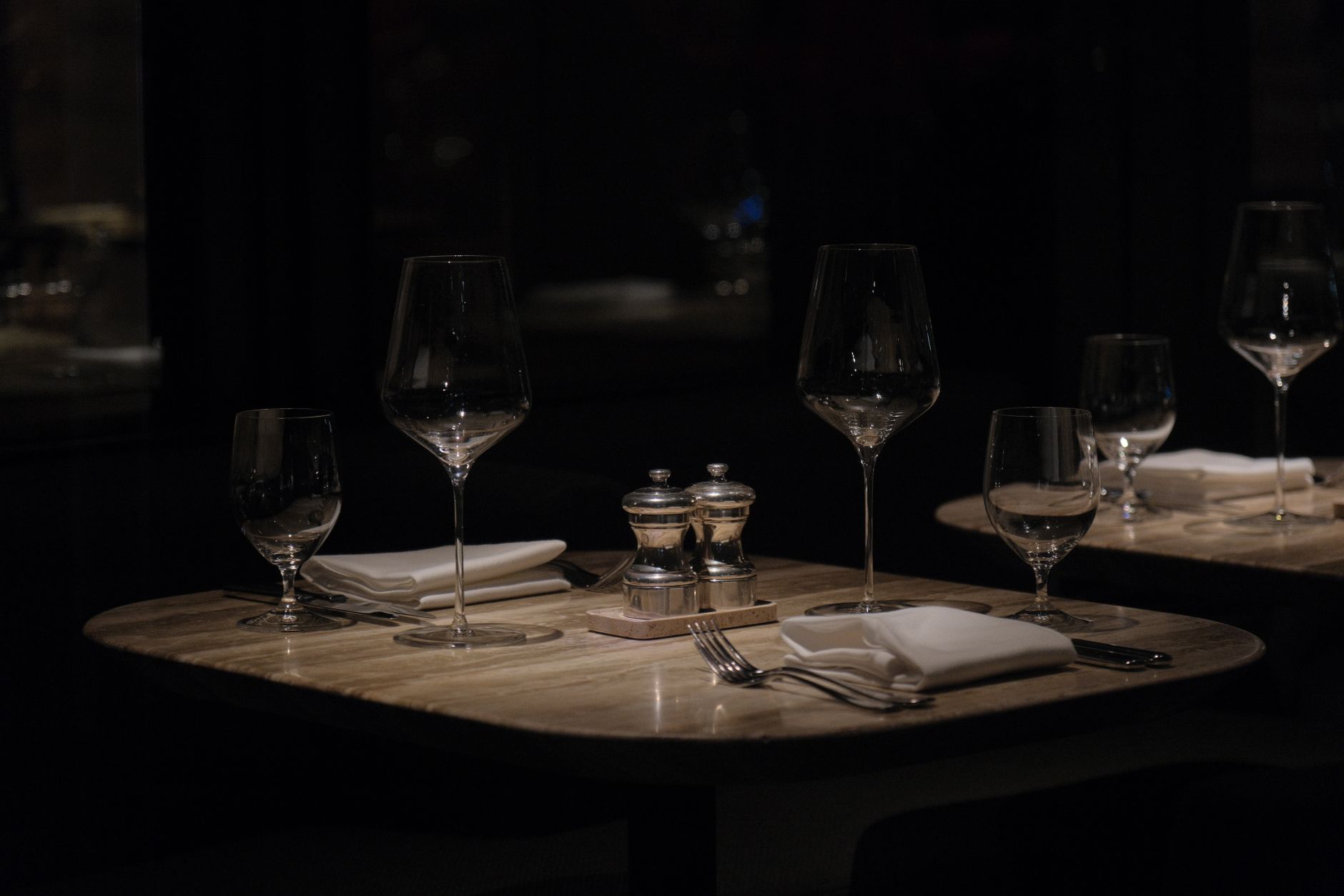 A dark, atmospheric restaurant table setup with wine glasses and napkins, creating a sophisticated ambiance.