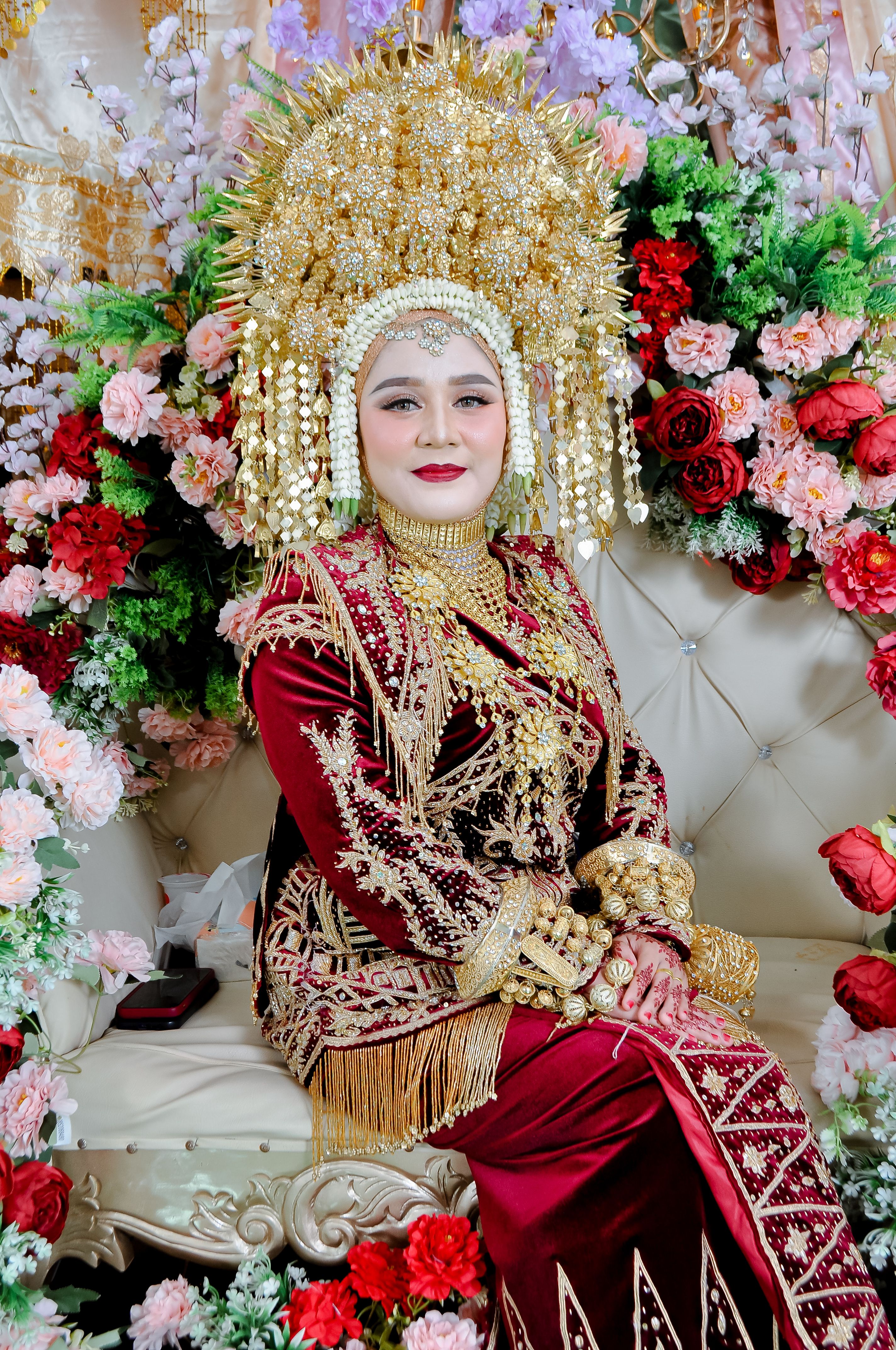 Woman in elaborate traditional wedding attire surrounded by vibrant flowers.