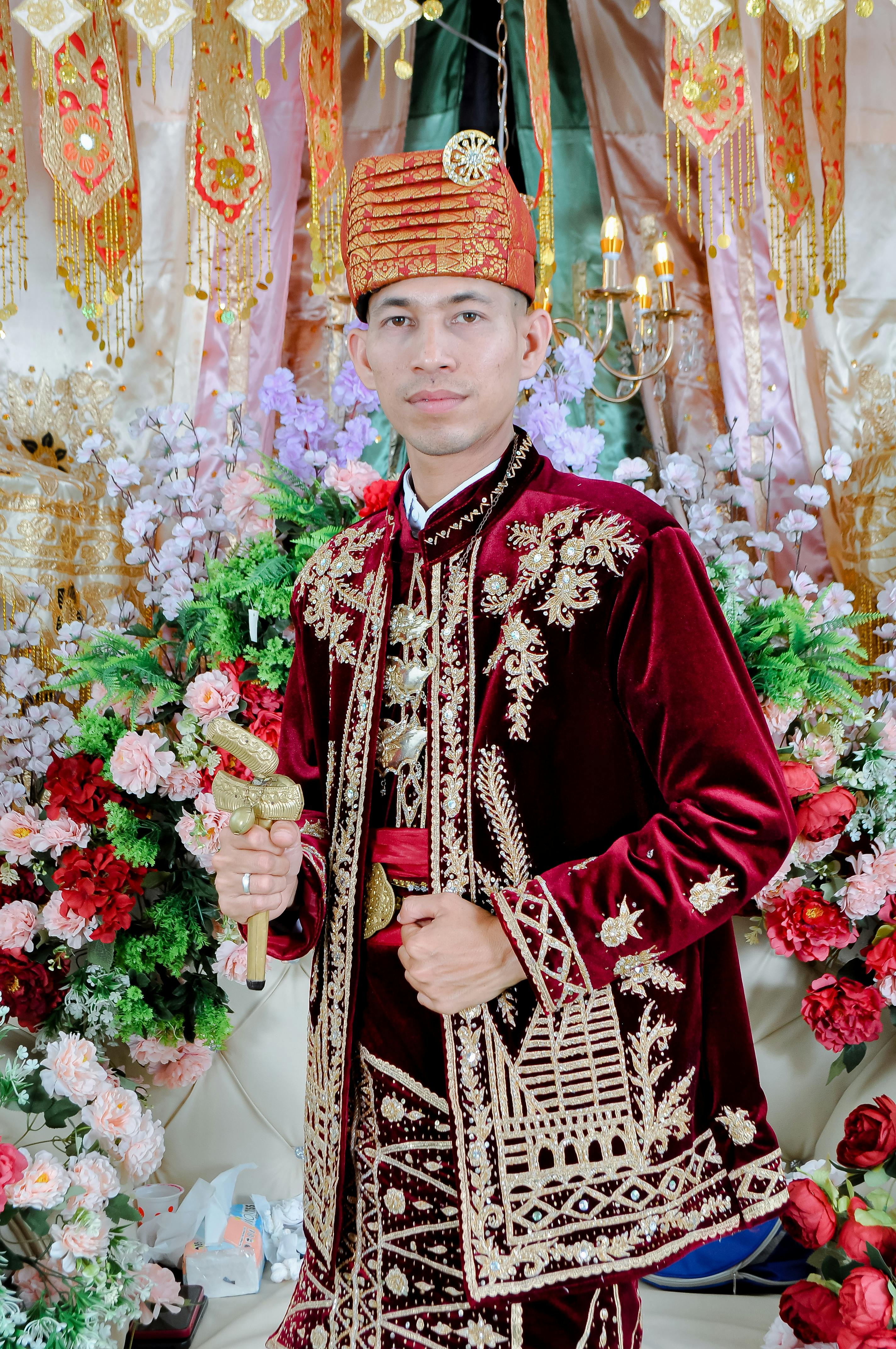 Portrait of a groom in traditional ornate red attire surrounded by vibrant flowers