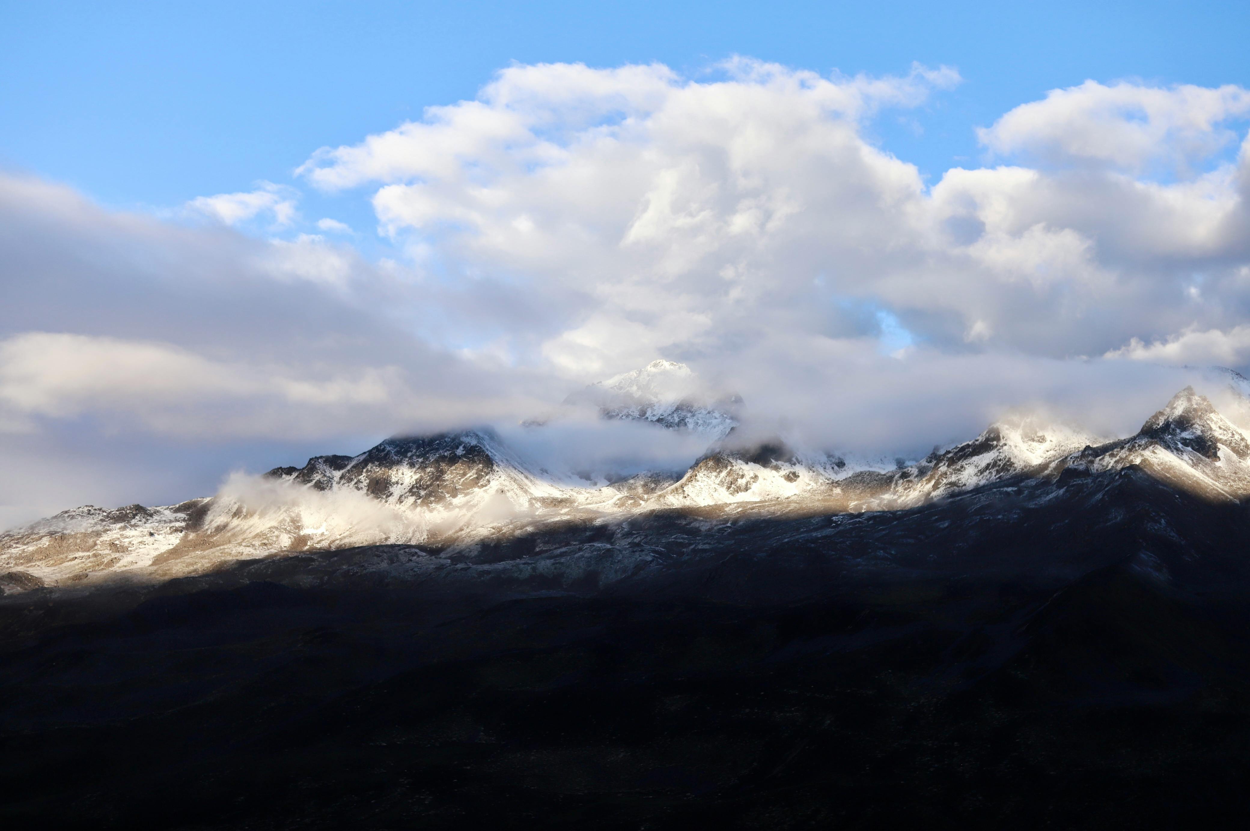 Breathtaking view of snow-capped mountains emerging through clouds at sunrise, showcasing nature