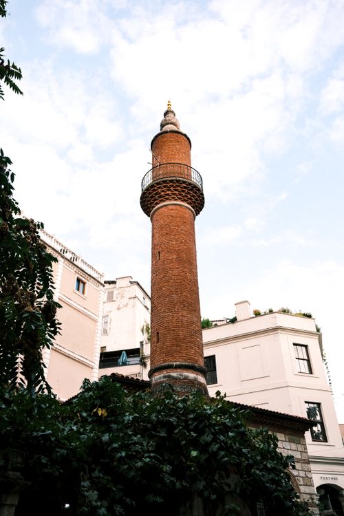 Free A red brick minaret stands tall against a bright blue sky, surrounded by buildings and greenery. Stock Photo