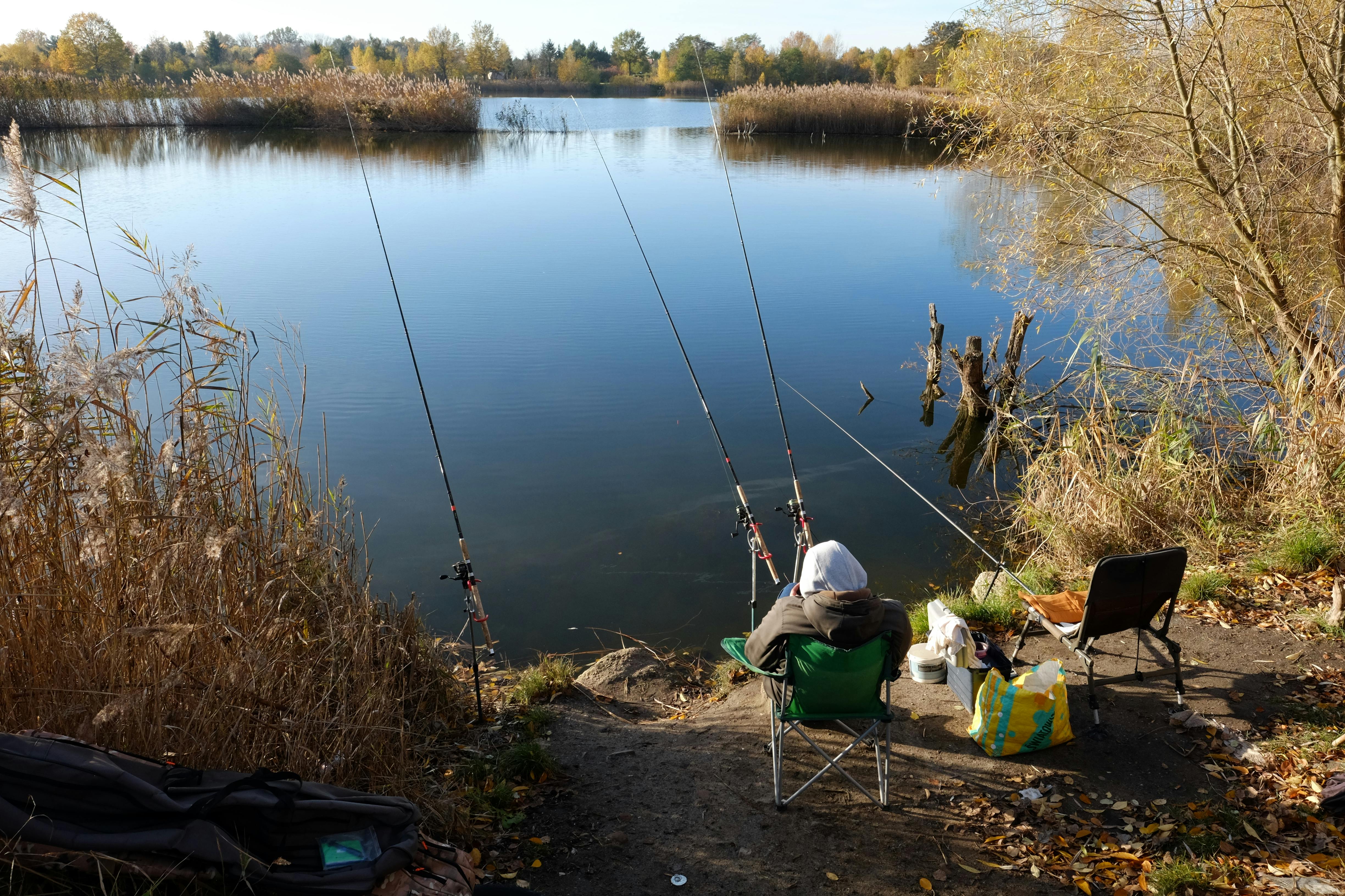A lone fisherman enjoys a peaceful afternoon at a serene lakeside in autumn.