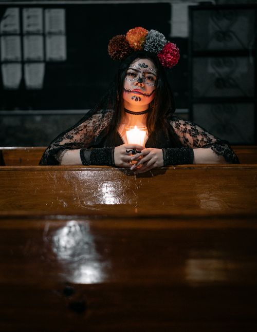 Free Woman with Day of the Dead face paint holding candle in dimly lit room. Stock Photo