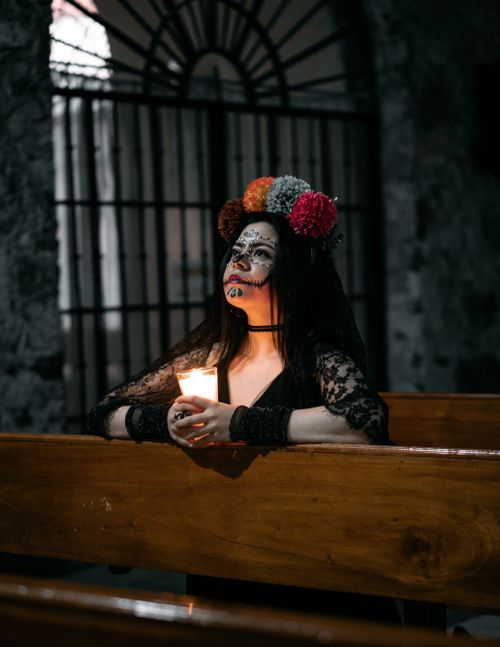 Free A woman with Day of the Dead makeup holds a candle in a church, symbolizing contemplation. Stock Photo