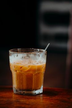 Close-up of a refreshing iced coffee in a clear glass with straw on a wooden table.