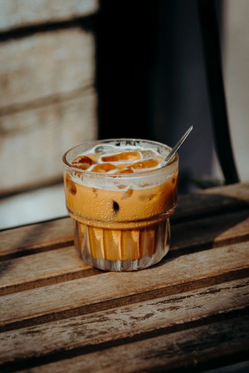 Free Chilled iced coffee in a glass with spoon on a sunlit wooden table, perfect summer refreshment. Stock Photo