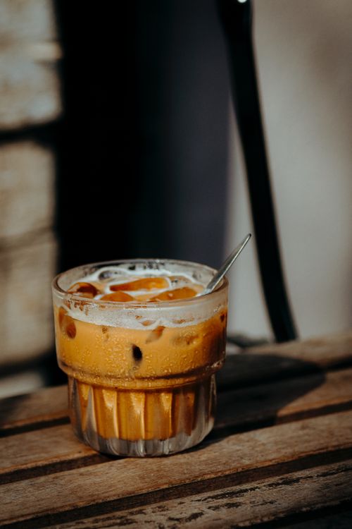 Free Refreshing iced coffee served in a glass with a metal spoon on a wooden table in natural lighting. Stock Photo