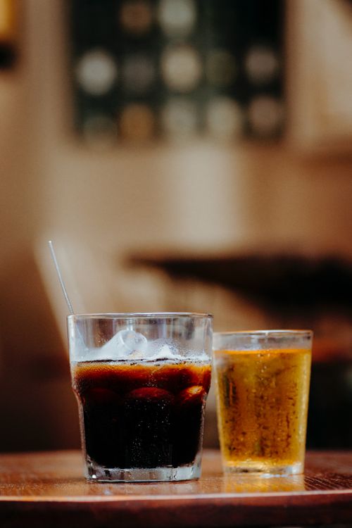 Free Close-up of cola and beer glasses on a wooden table in a cozy indoor setting. Stock Photo
