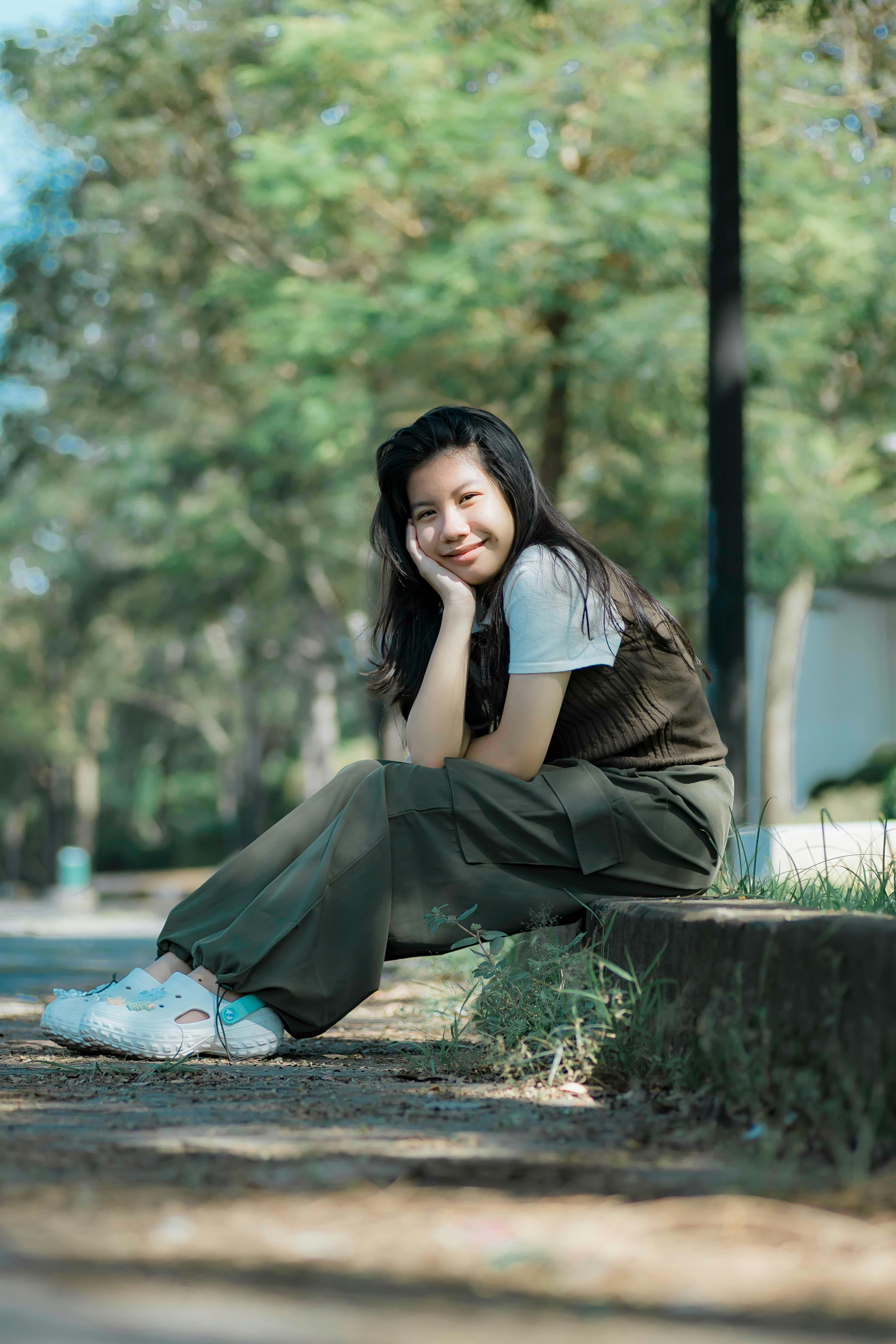 Gratis Giovane donna sorridente seduta all'aperto nel parco, che si gode una giornata di sole. Foto a disposizione