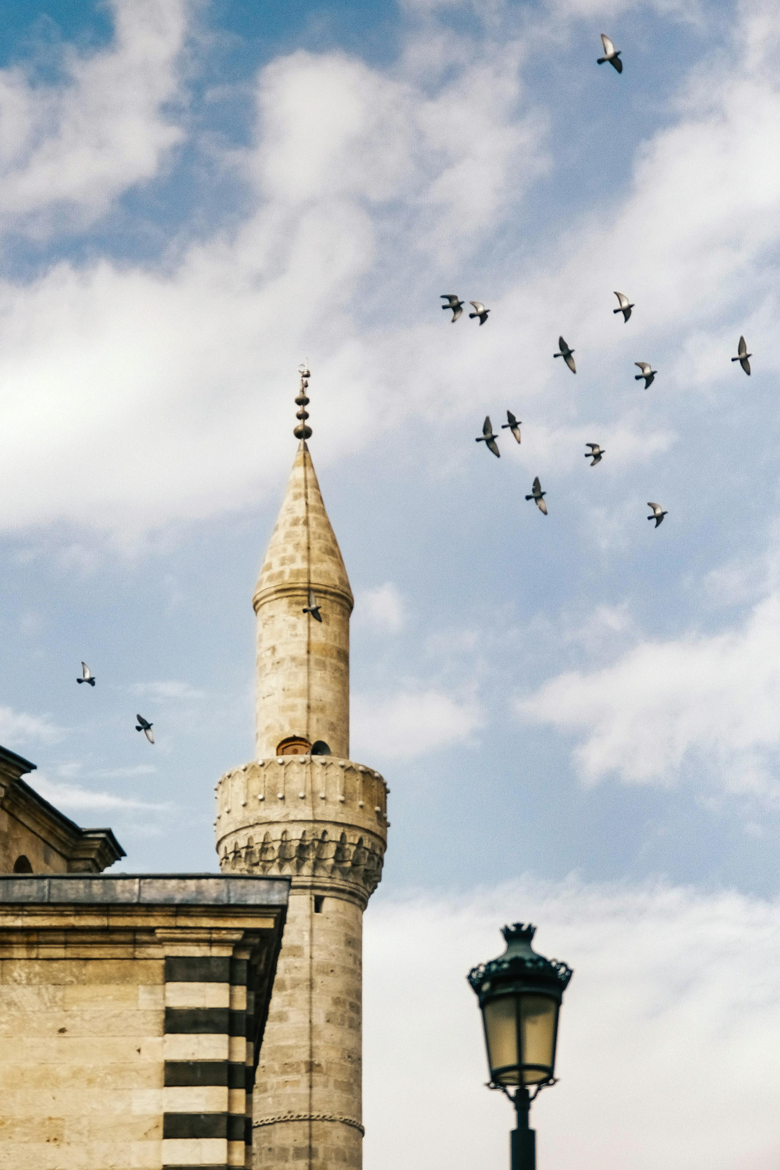 Majestic minaret with birds flying against a clear blue sky.