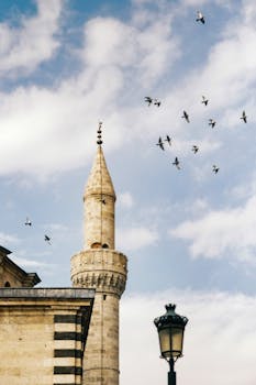 Majestic minaret with birds flying against a clear blue sky.