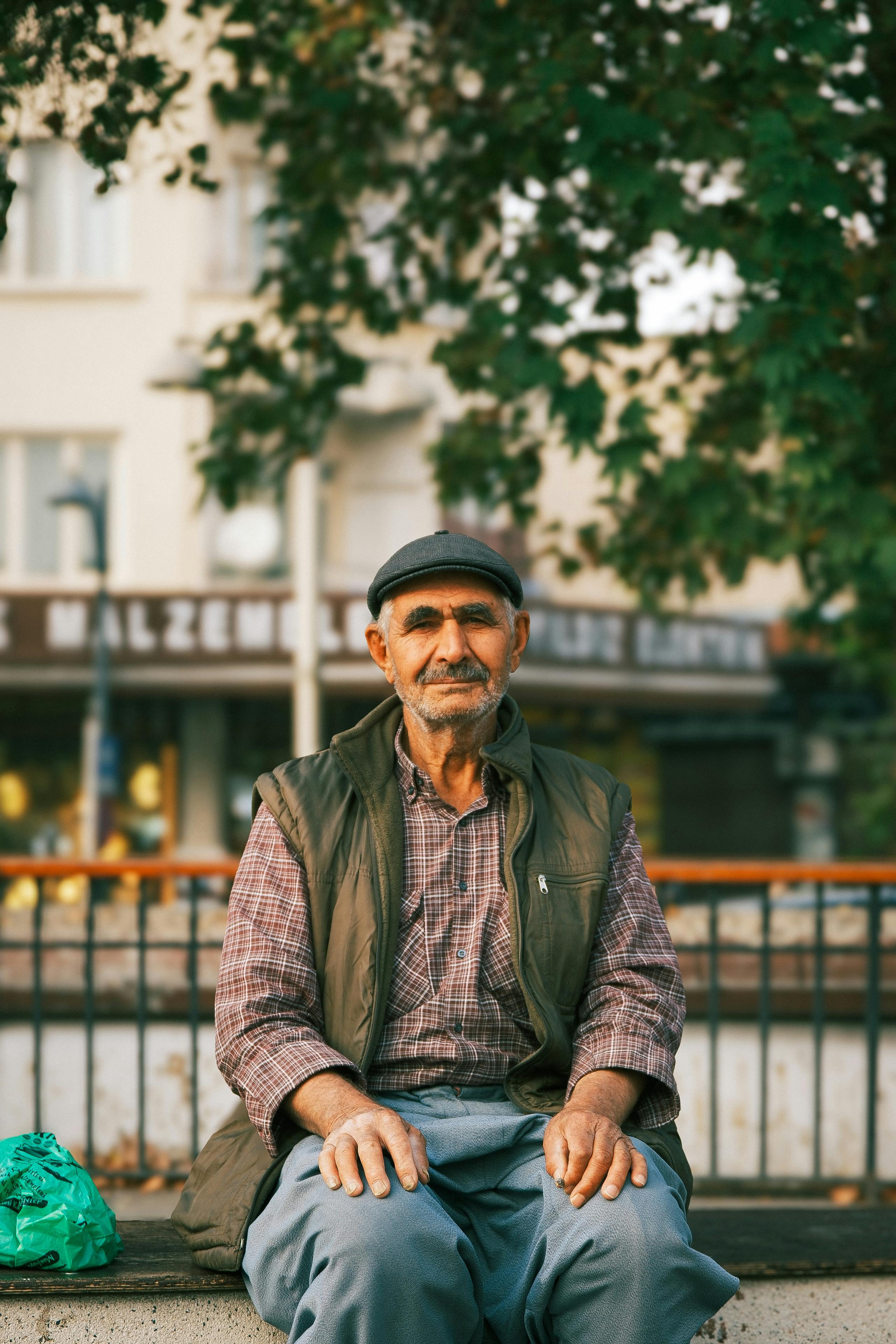 Elderly man sitting on a bench in an urban park with trees around.