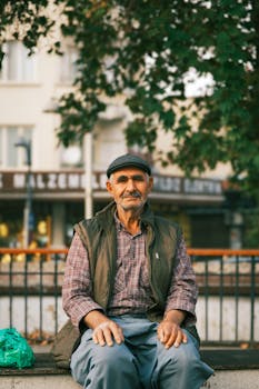 Elderly man sitting on a bench in an urban park with trees around.
