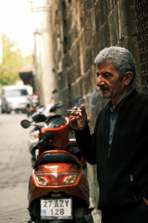 Free Older man smoking in a narrow European street with scooters and old walls. Stock Photo