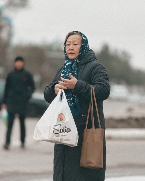 Free Elderly woman holding shopping bags, standing on a Tashkent street, dressed warmly for winter. Stock Photo