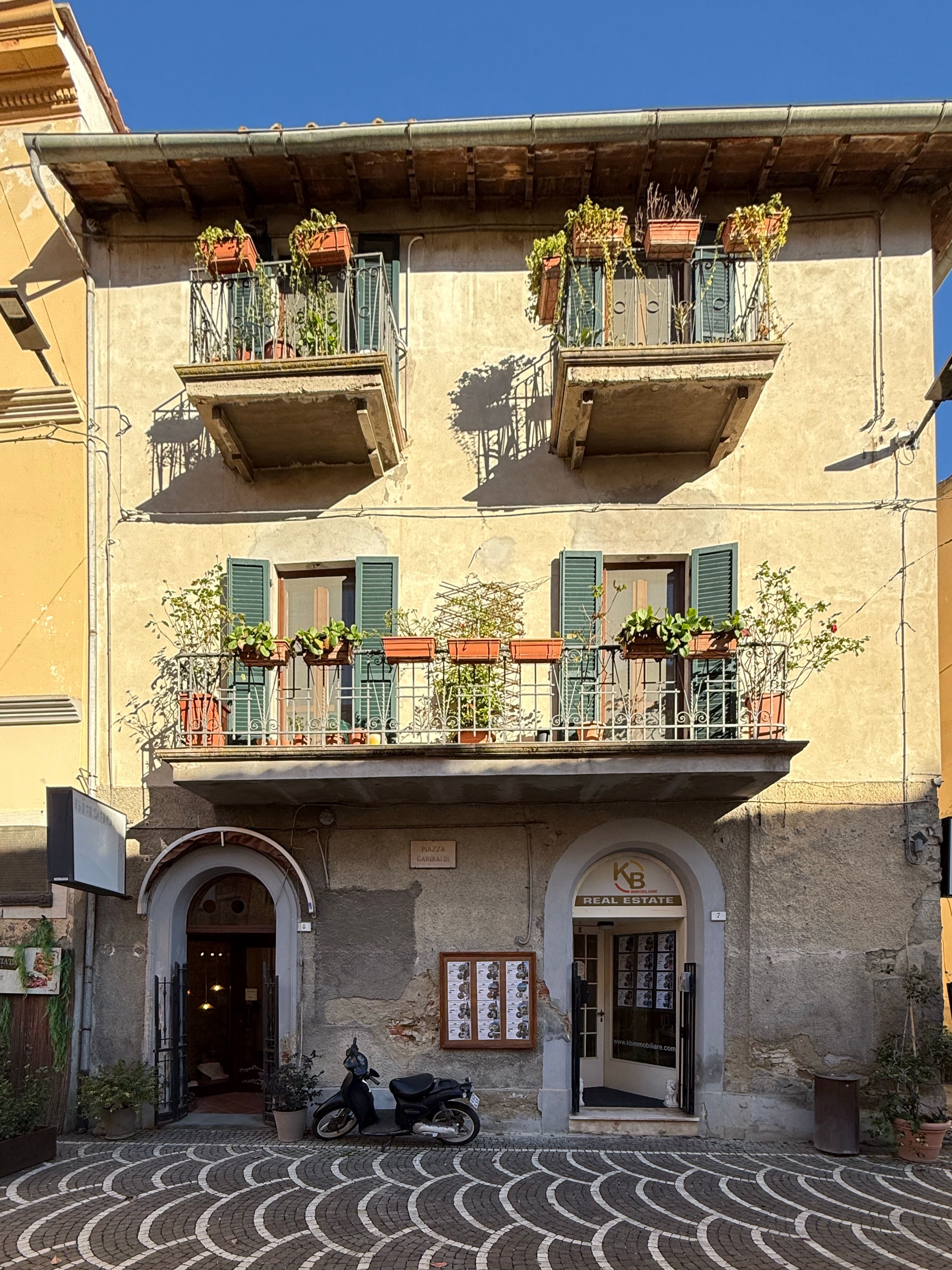 Gratis Un pittoresco edificio italiano con piante in vaso sui balconi sotto un cielo azzurro e limpido. Foto a disposizione
