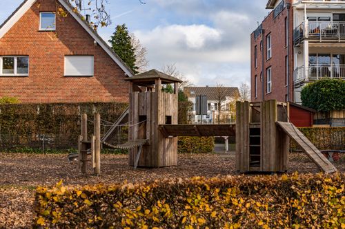 Free A cozy suburban playground featuring a wooden play structure surrounded by autumn foliage and residential buildings. Stock Photo