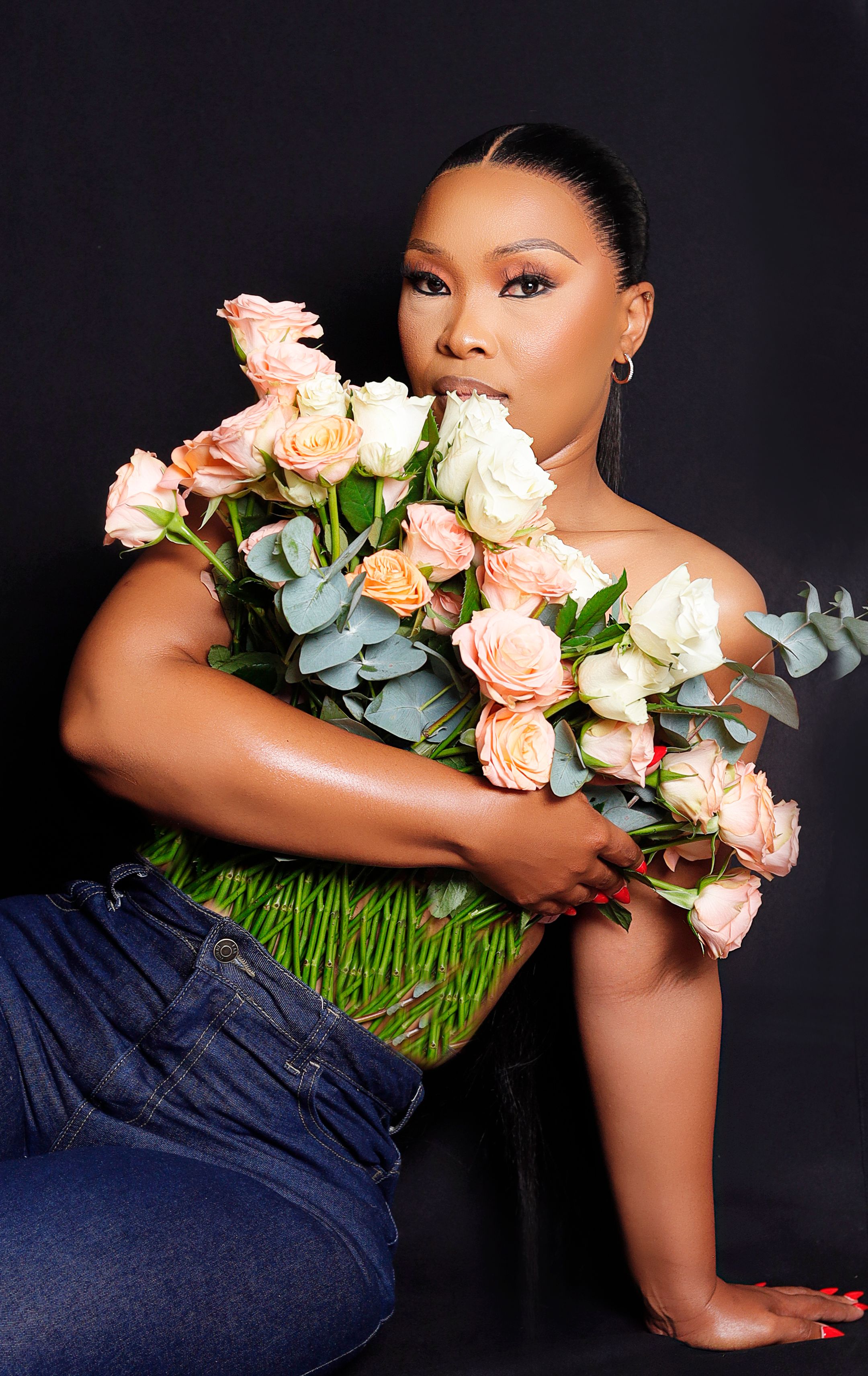 Striking portrait of a woman embracing a vibrant floral arrangement against a black background.