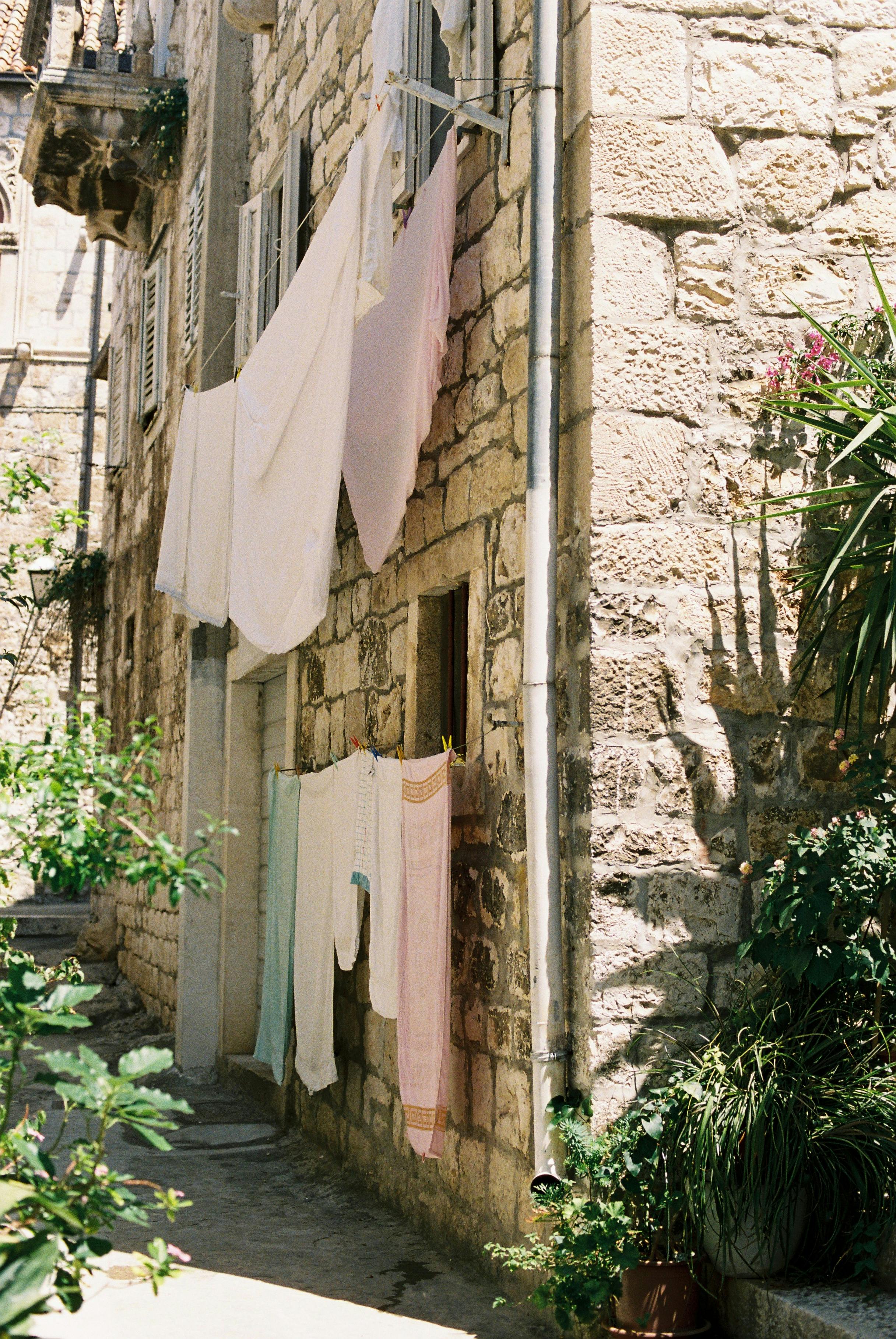 Rustic stone building with clothesline and greenery in a quaint alley.