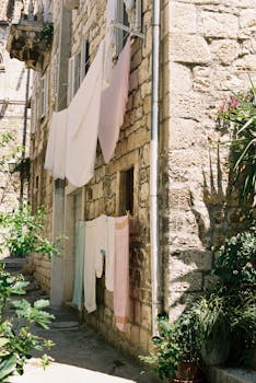 Rustic stone building with clothesline and greenery in a quaint alley.