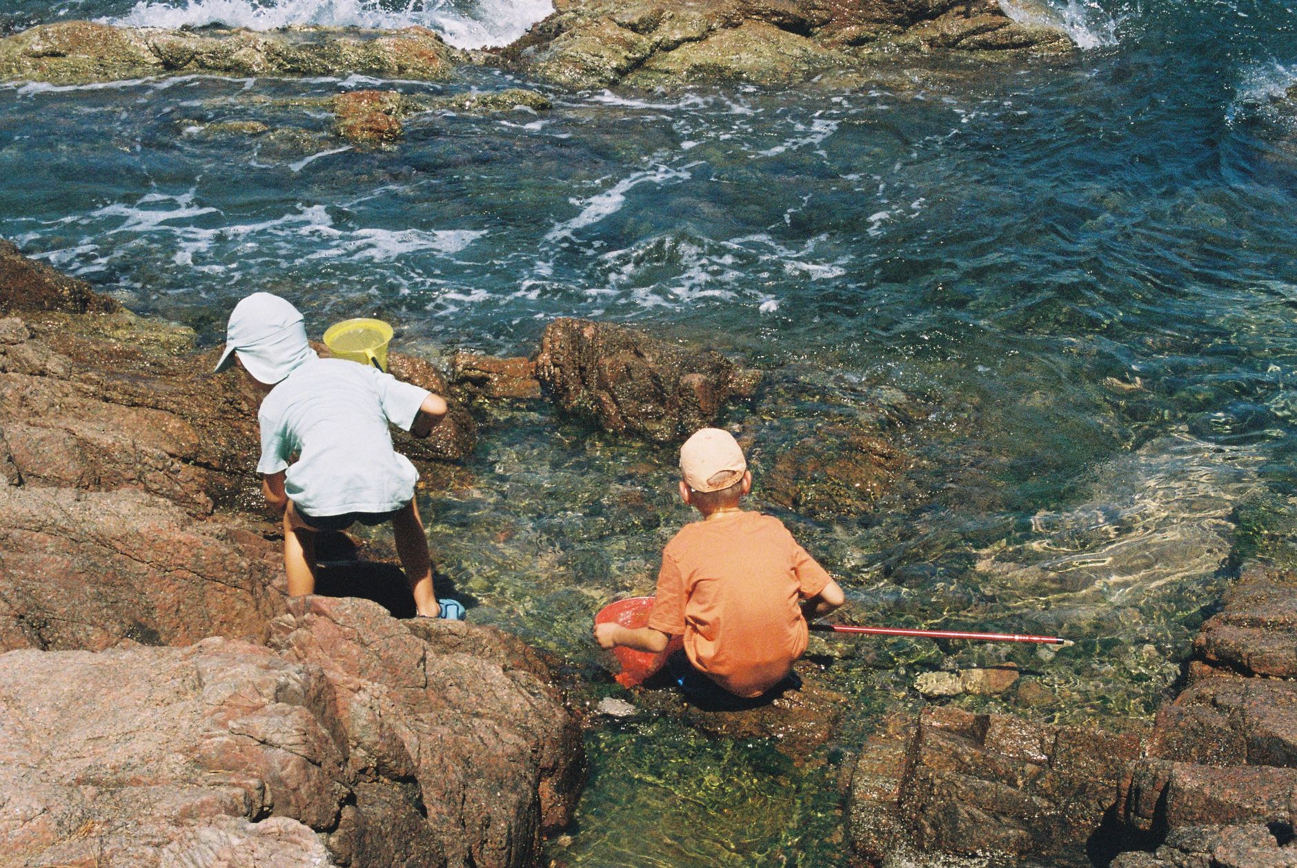 澎湖親子生態景點:潮間帶、濕地與海洋教育體驗全指南 Two children playing and exploring tide pools on a rocky seashore during daytime.