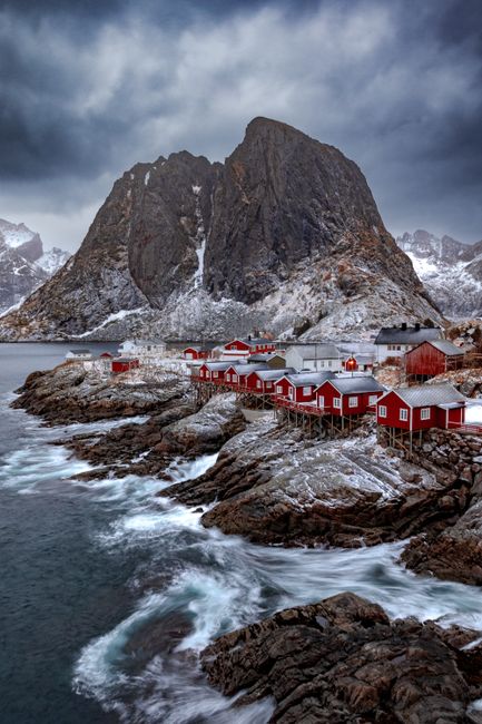 Dramatic landscape of red cabins and mountains in snowy Lofoten, Norway.