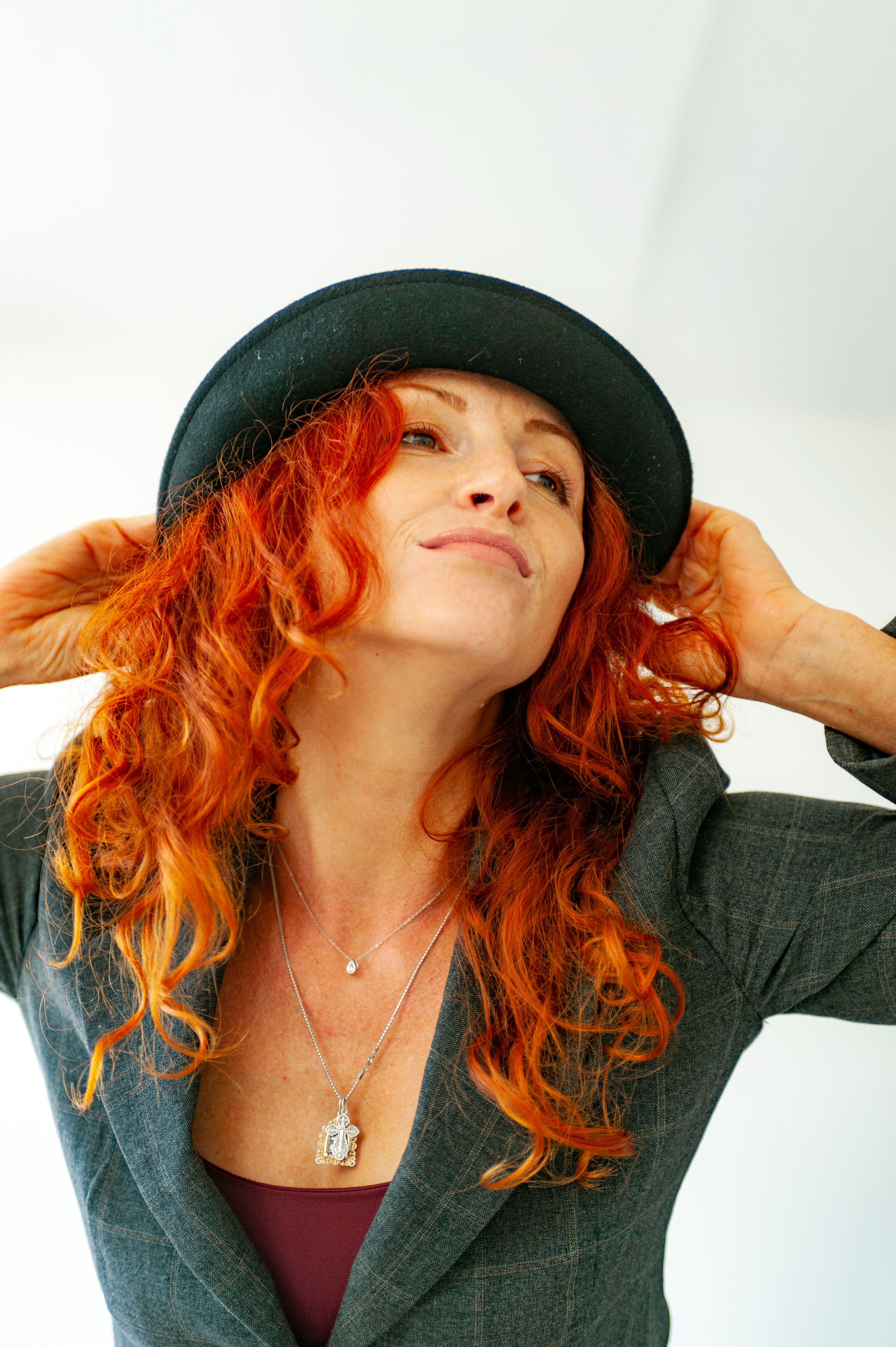 Portrait of a confident woman with vibrant red hair wearing a stylish hat and gray jacket.