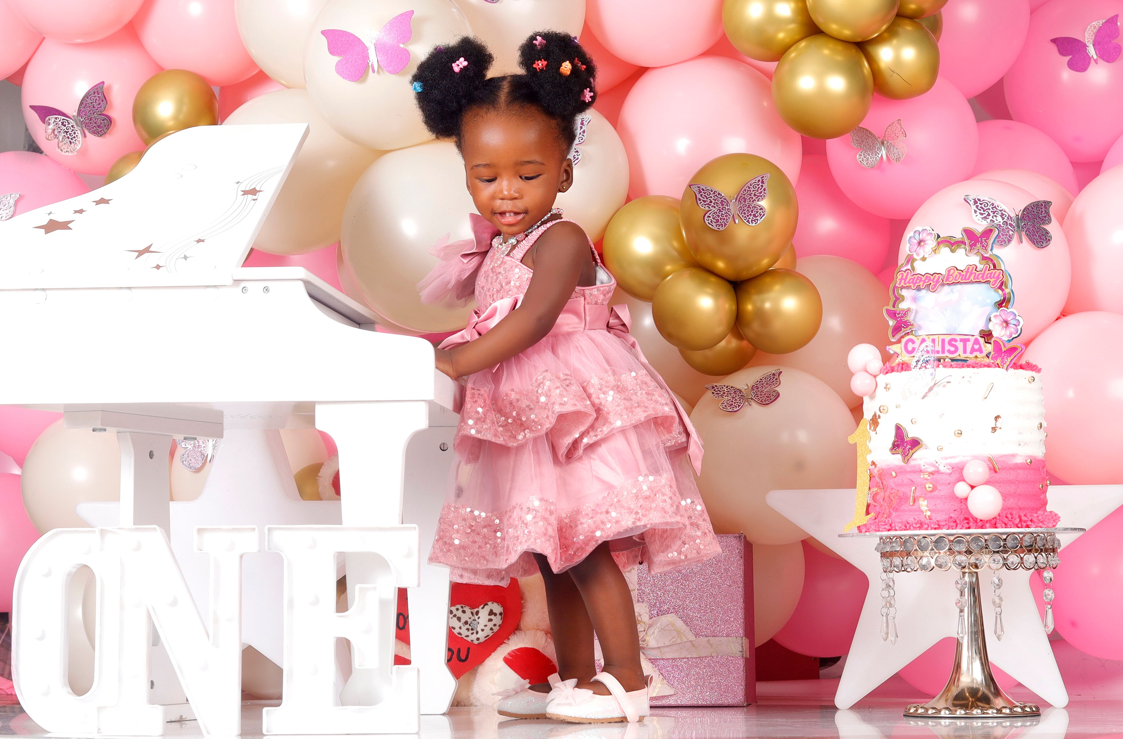 Cute child in pink celebrating first birthday with piano and balloons.