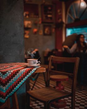 Warm interior of a café with a steaming coffee cup on a wooden table, creating a cozy ambiance.