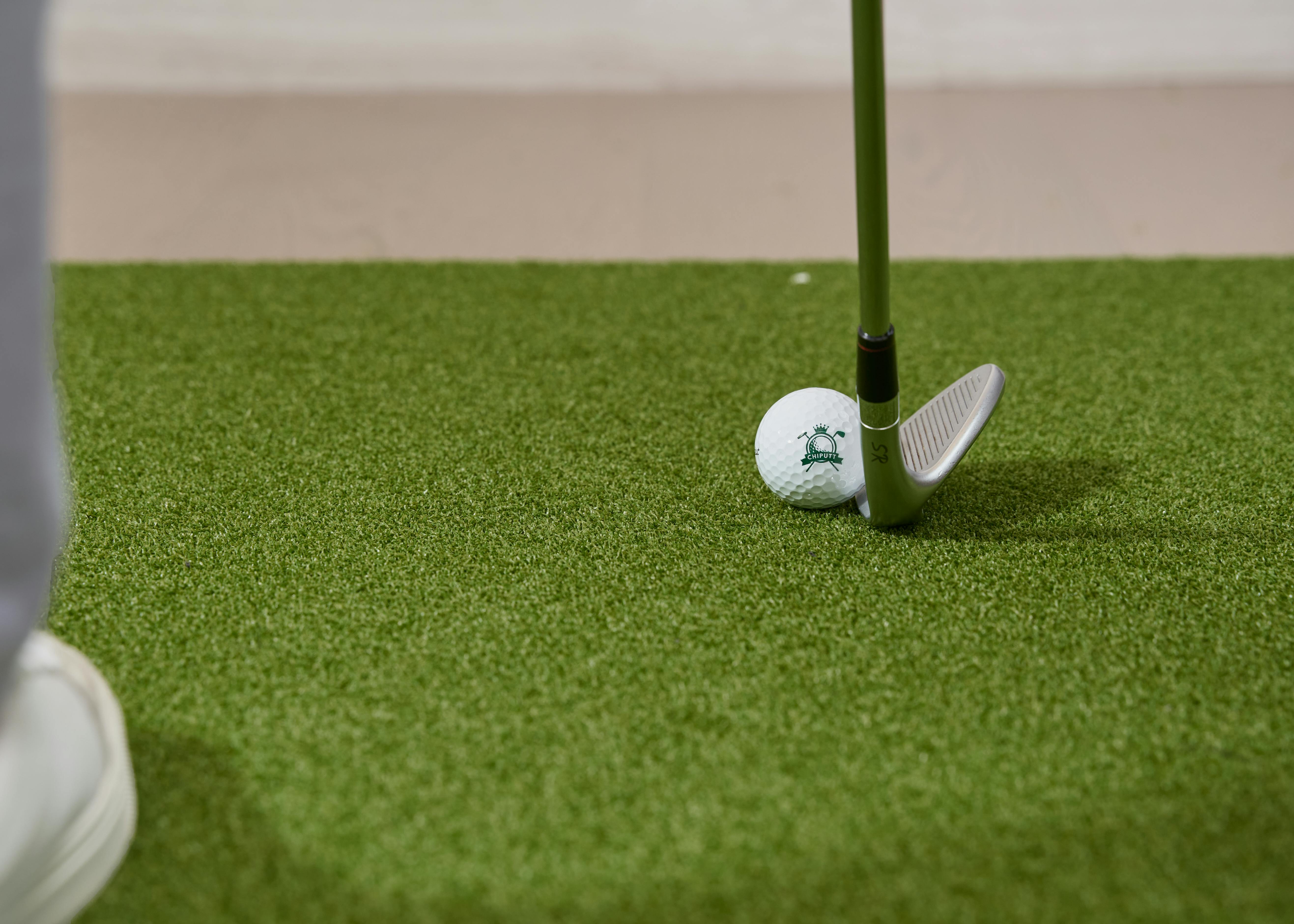 A detailed shot of a golf club and ball positioned on artificial turf. Perfect for golf training themes.