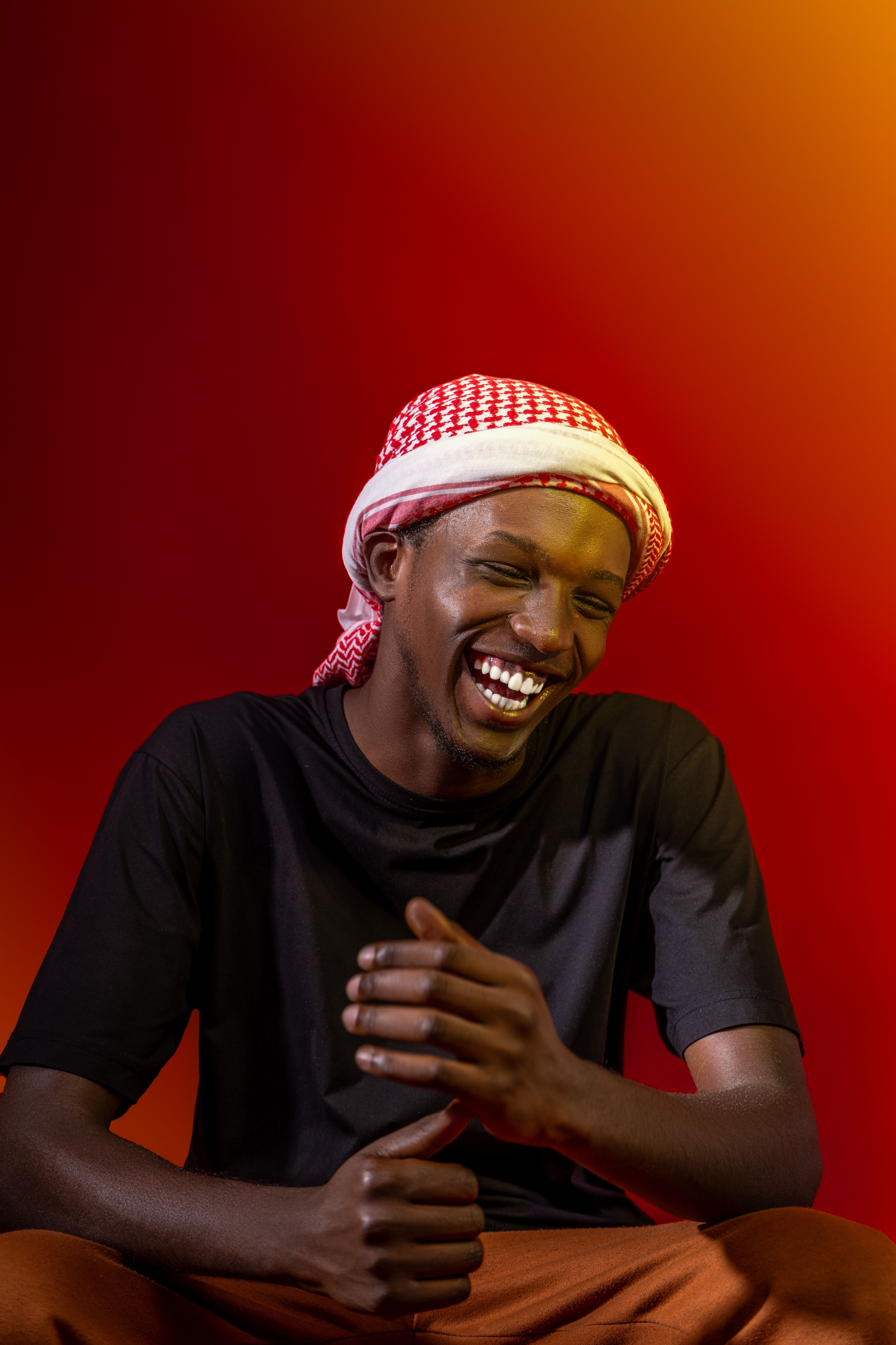 A joyful portrait of an adult man laughing, set against a colorful gradient background in Rwanda.