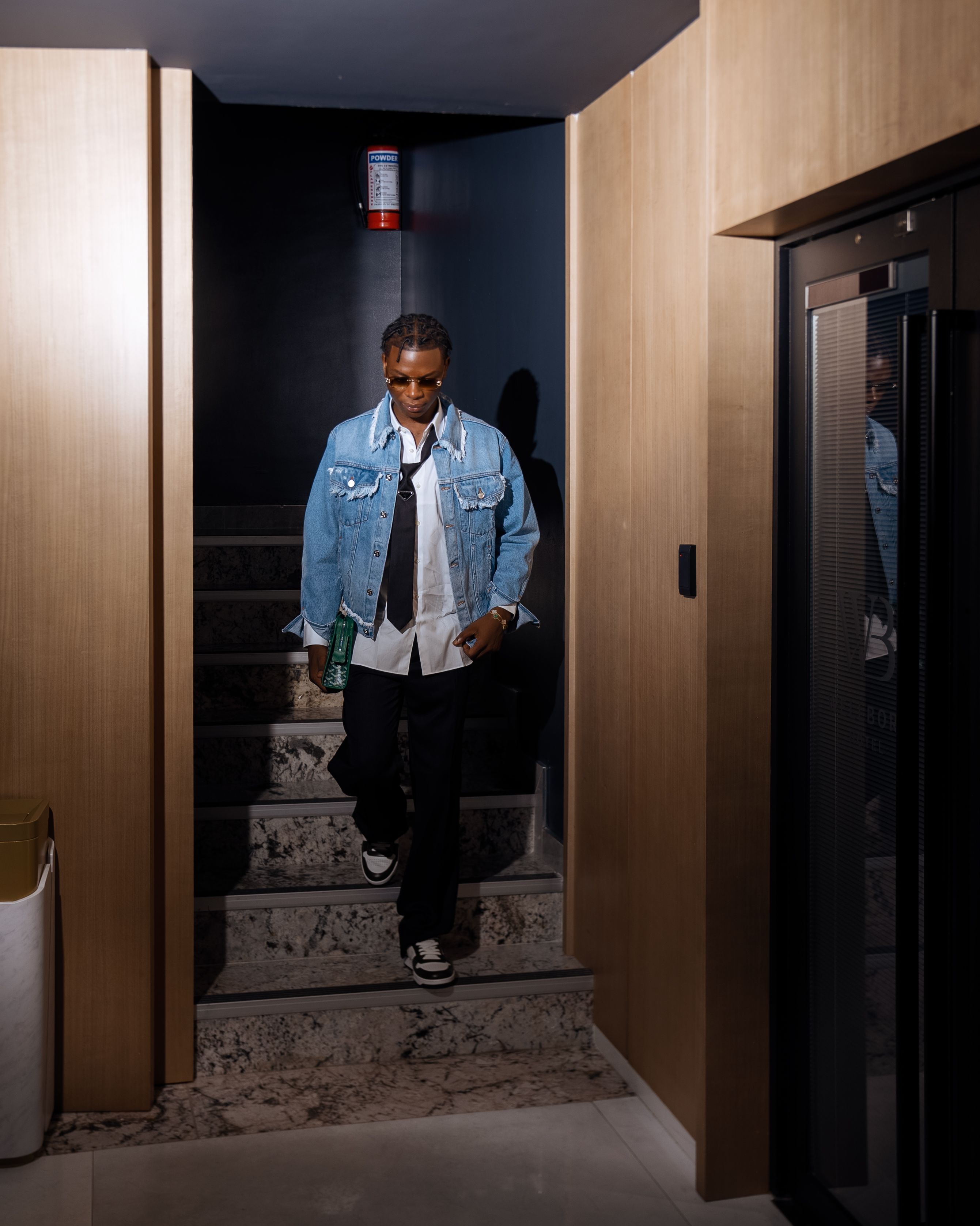 Fashionable young adult in denim jacket descends stairs. Indoor modern setting.