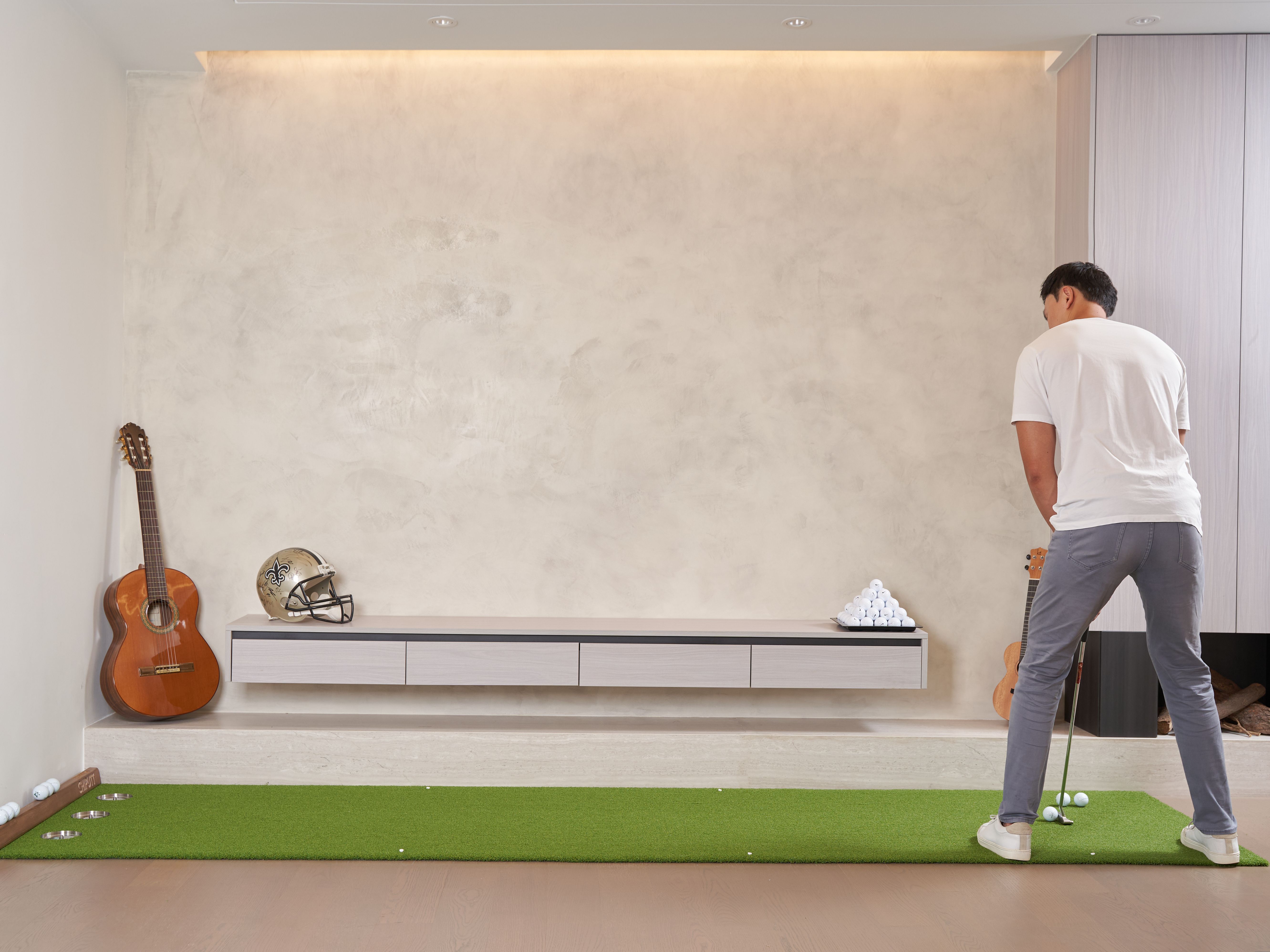 Man practicing golf indoors using a putting mat surrounded by decor.