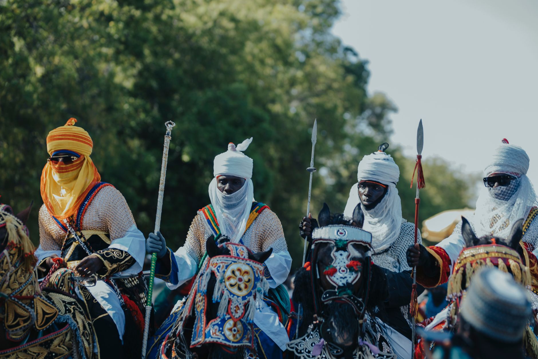 Vibrant African horsemen in traditional attire with spears display cultural heritage outdoors.