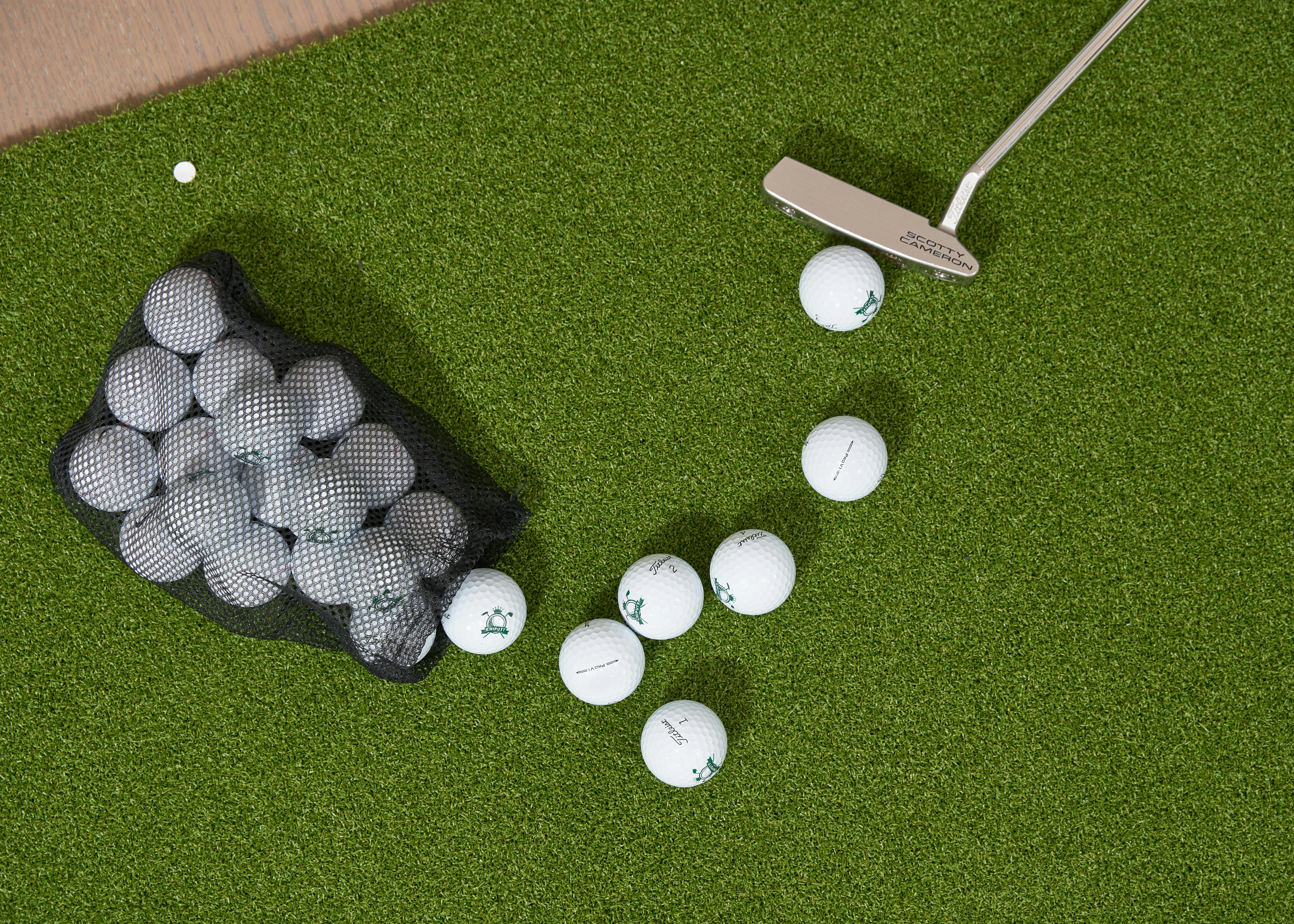 Overhead shot of golf balls, putter, and bag on a putting green turf.