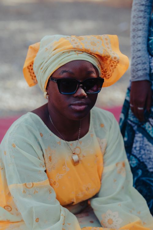 Free A woman in vibrant traditional African attire and sunglasses enjoying an outdoor event in daylight. Stock Photo