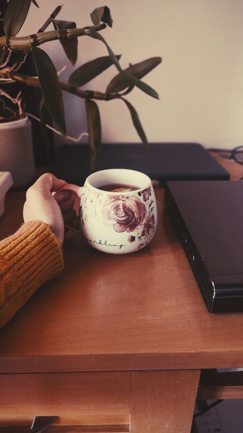 Free A comforting cup of tea held near a laptop in a cozy home office scene. Stock Photo