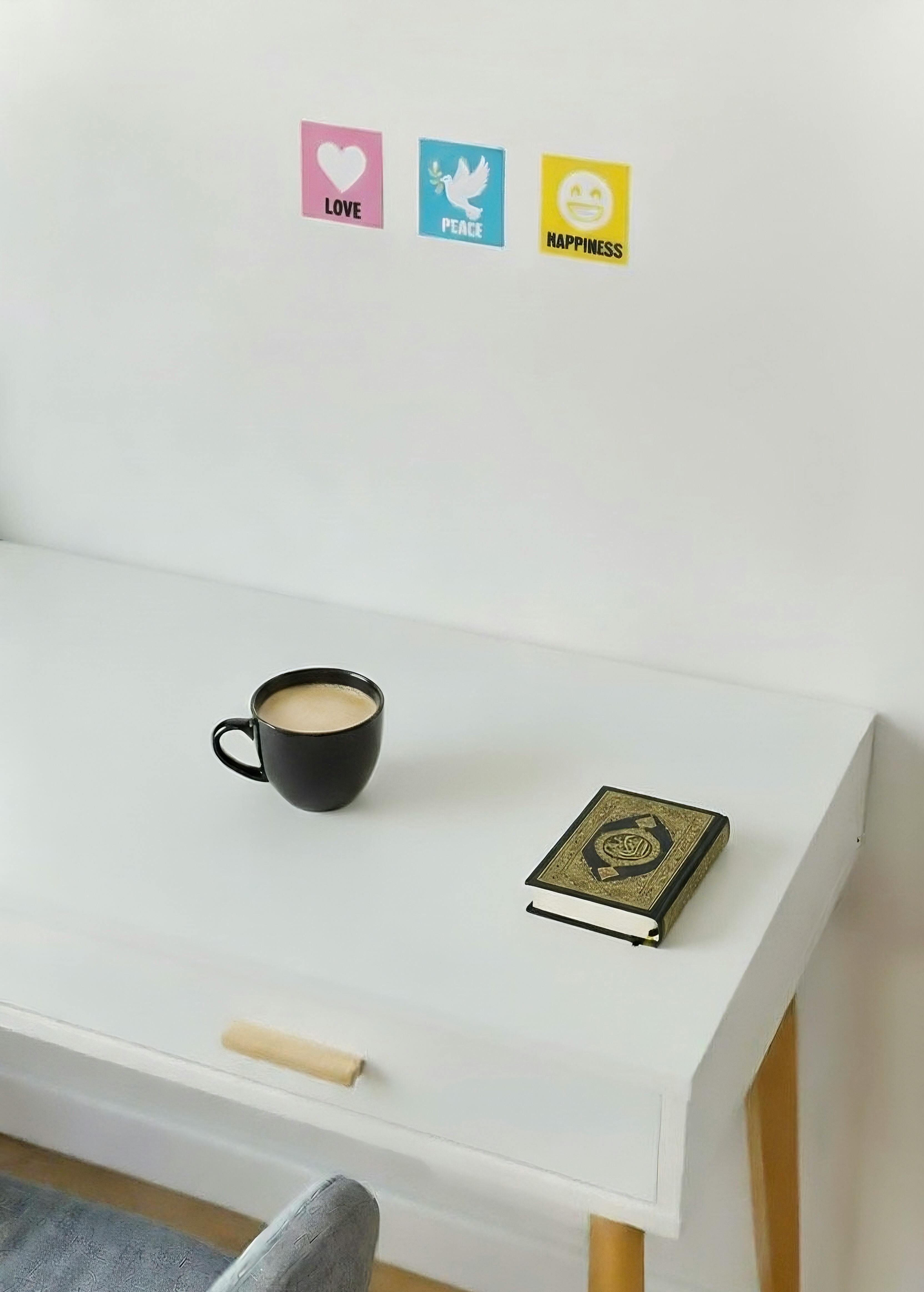 Gratis Et rolig arbeidsområde med en Koran, en kaffekopp og motivasjonsplakater som fremmer kjærlighet, fred og lykke. Arkivbilde