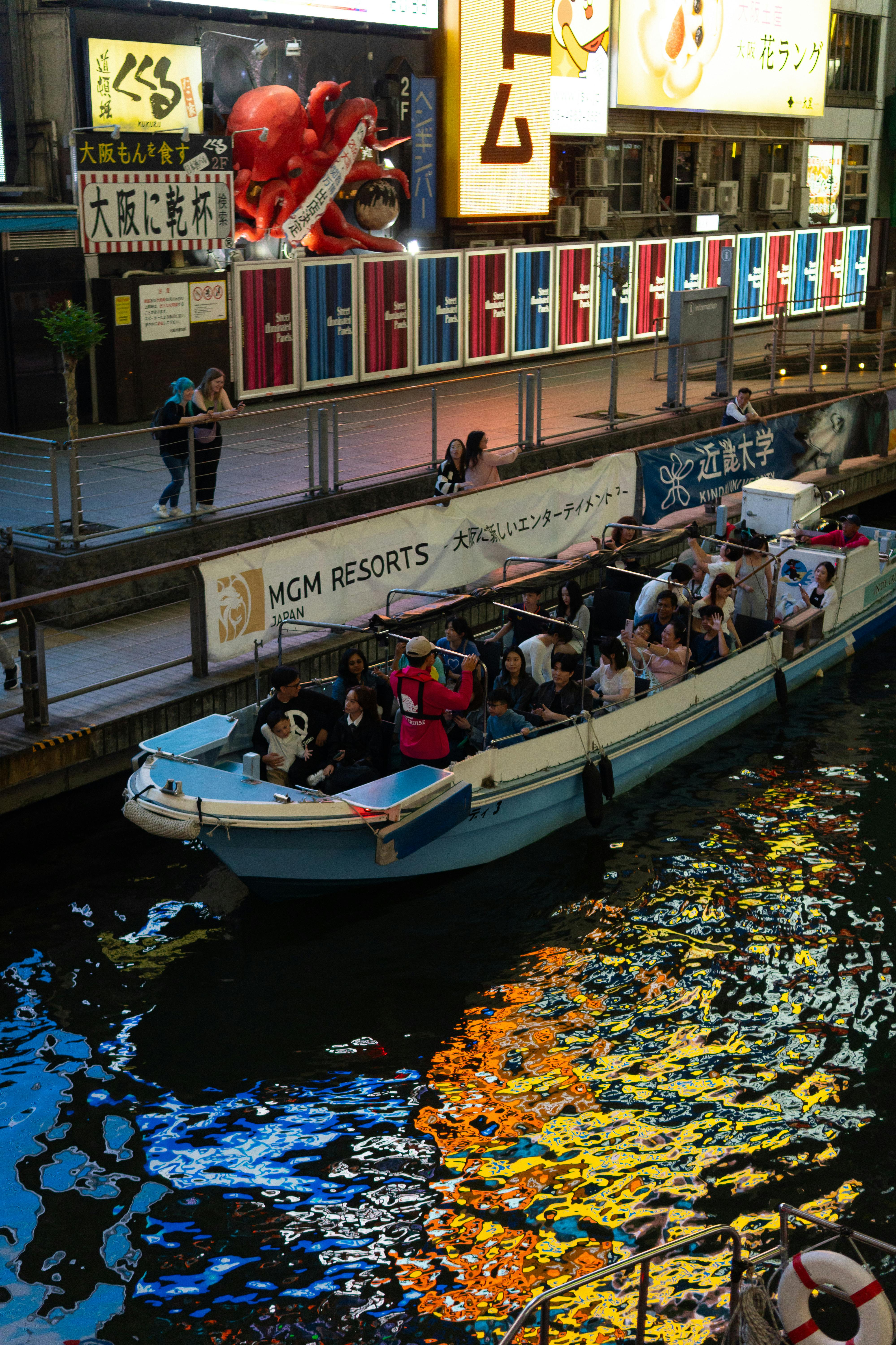 Vibrant canal boat ride with tourists in Dotonbori, Osaka, Japan.