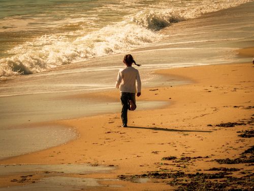 Free A child plays on a sunny beach with waves gently crashing onto the shore, capturing a carefree moment. Stock Photo