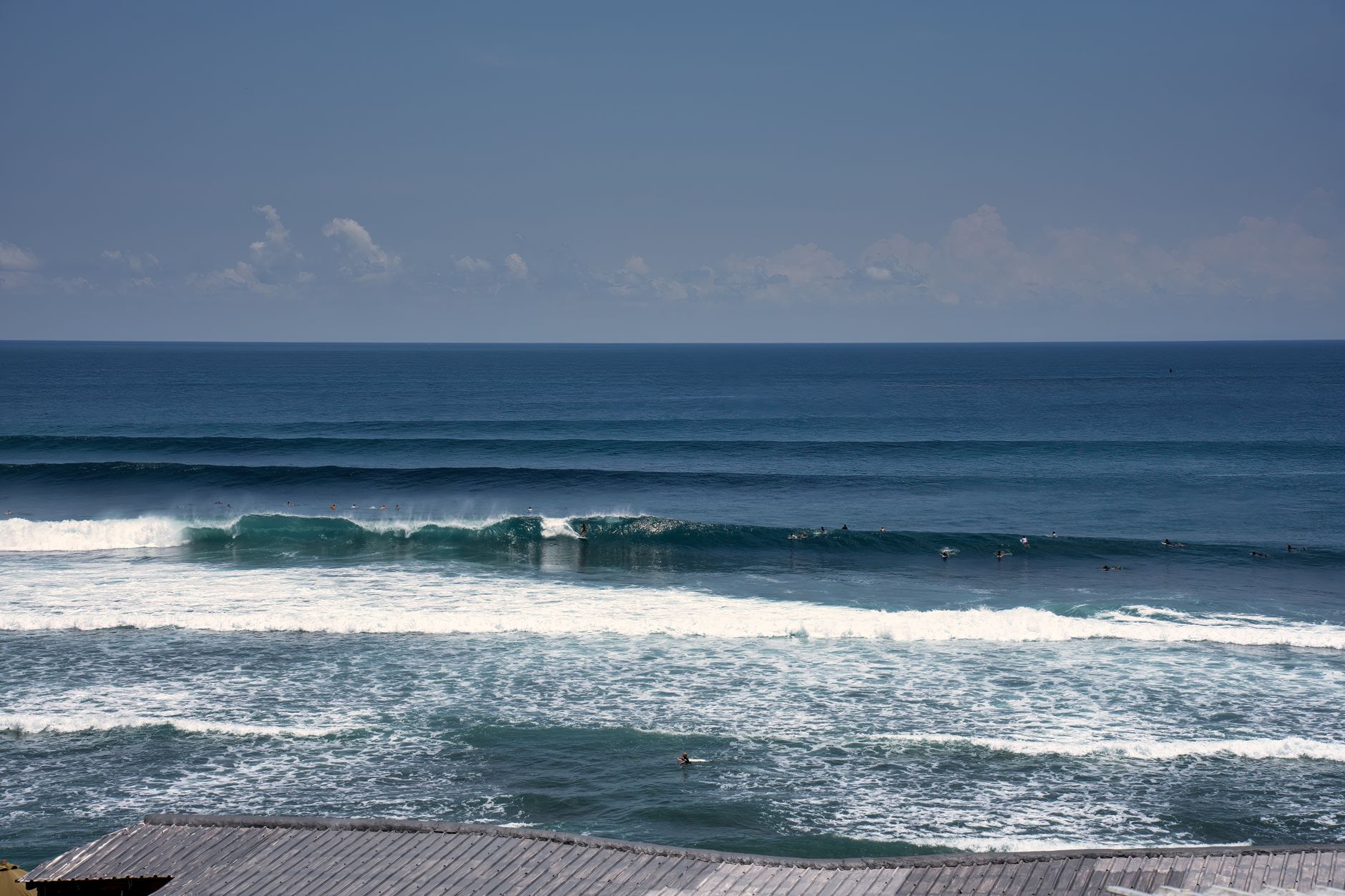 Surfers riding waves on a sunny day in Bali, Indonesia with clear blue ocean views.