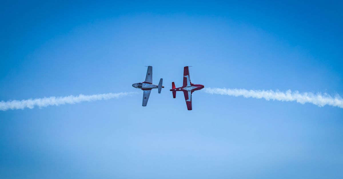 Two aerobatic planes performing a synchronized aerial maneuver against a clear blue sky.