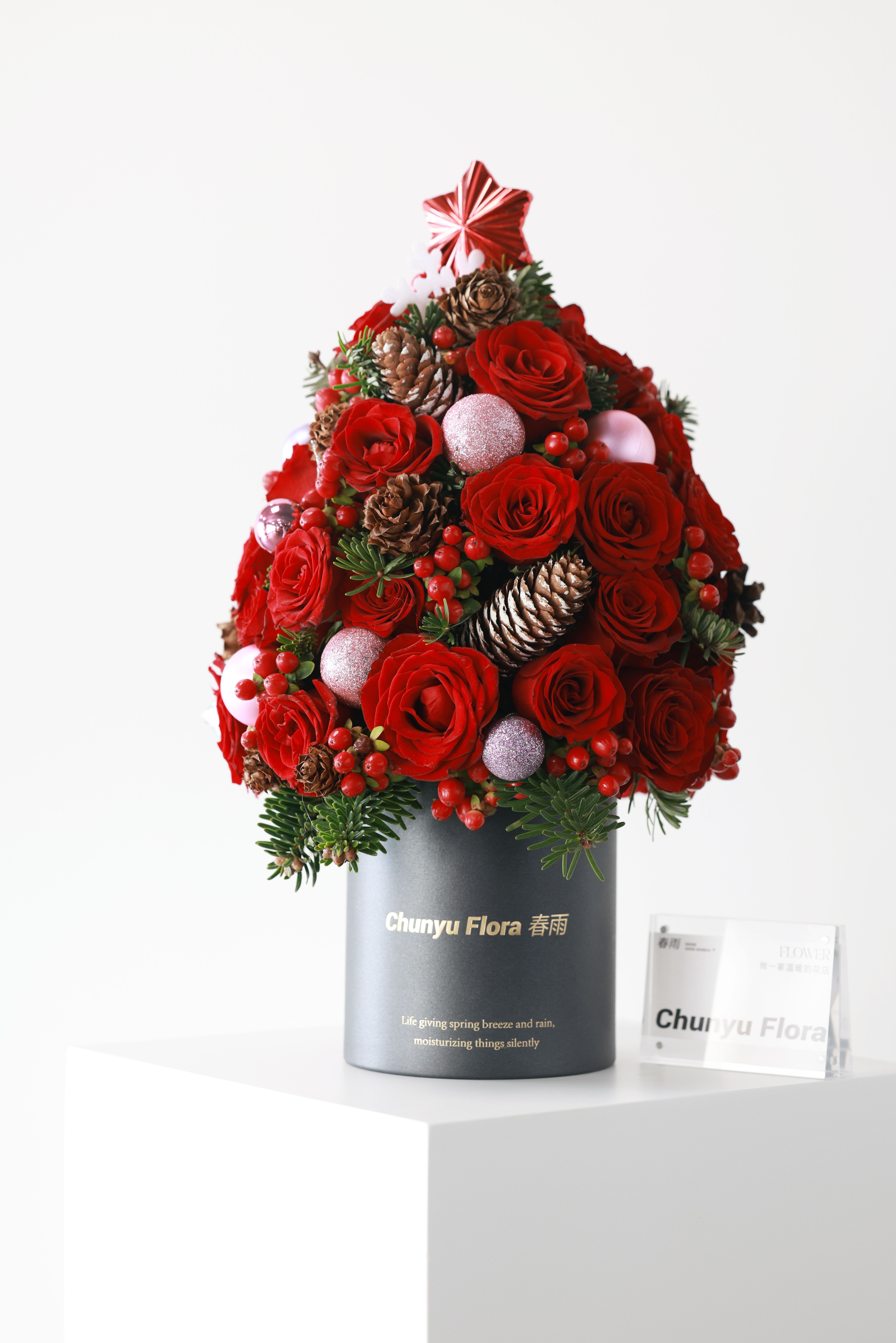 A festive Christmas floral arrangement featuring red roses, pinecones, berries, and ornaments, perfect for holiday decor.