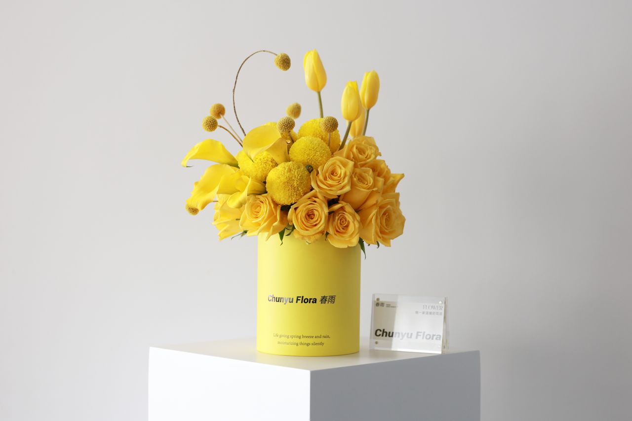 yellow flower arrangement with roses and tulips in a branded container