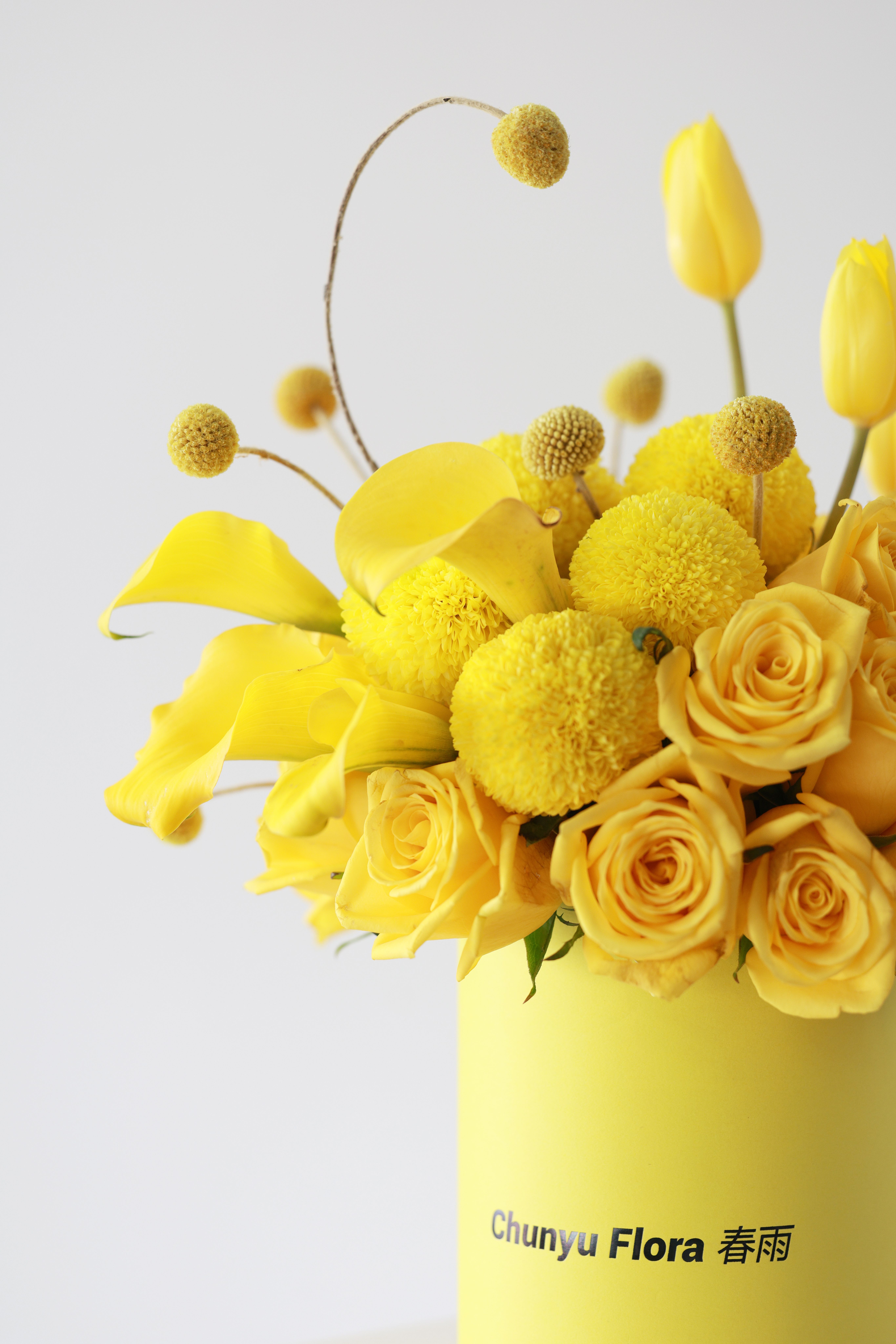 Vibrant yellow floral arrangement with roses, tulips, and text on vase.