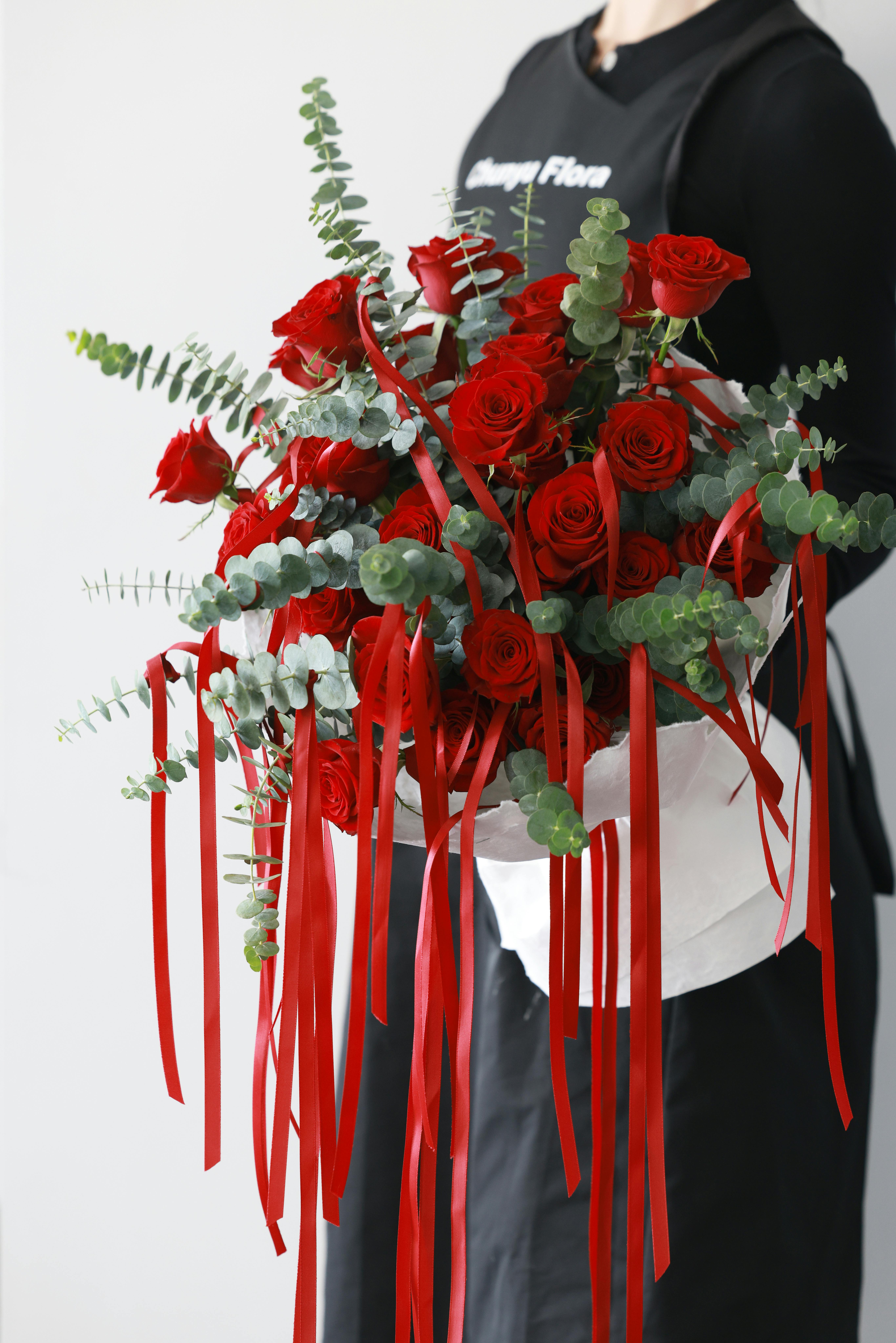 A beautiful bouquet featuring red roses and eucalyptus leaves, elegantly tied with red ribbons.