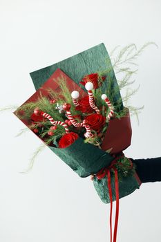 A Christmas-themed bouquet featuring red roses, green foliage, and candy cane decorations.