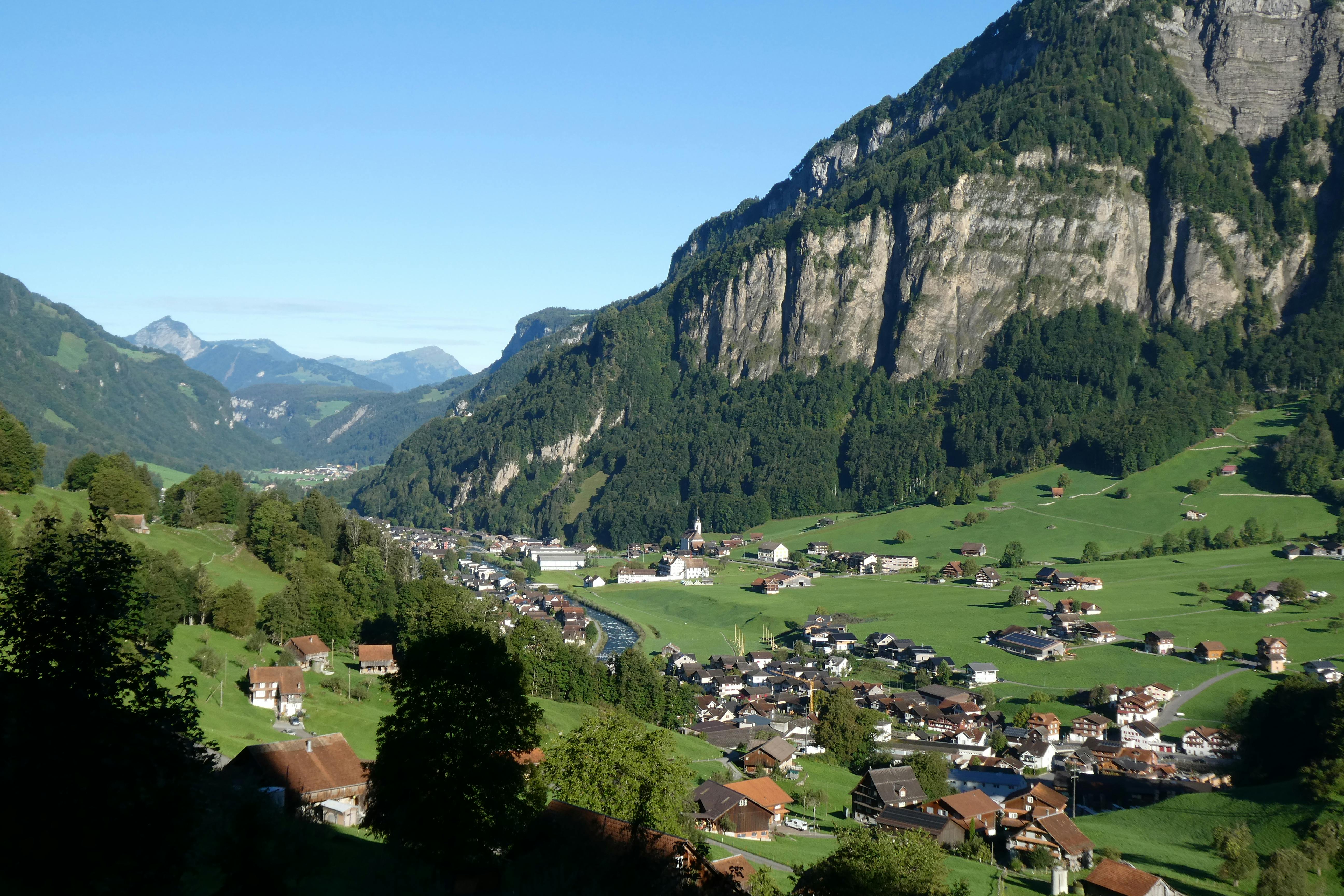 Scenic view of a Swiss village nestled in a lush mountain valley under a clear blue sky.