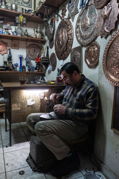 Free Artisan intricately engraves metal in a cozy workshop filled with ornate wall plaques. Stock Photo
